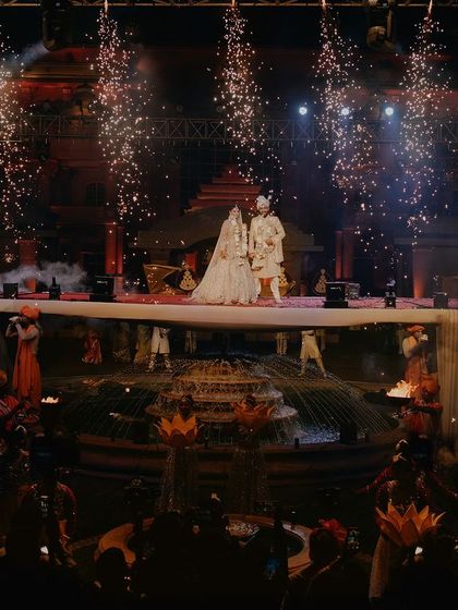A grand stage moment for Aditya and Megha, complete with fireworks and traditional performers. This shot captures the scale and theatricality of a lavish Sangeet or reception night.