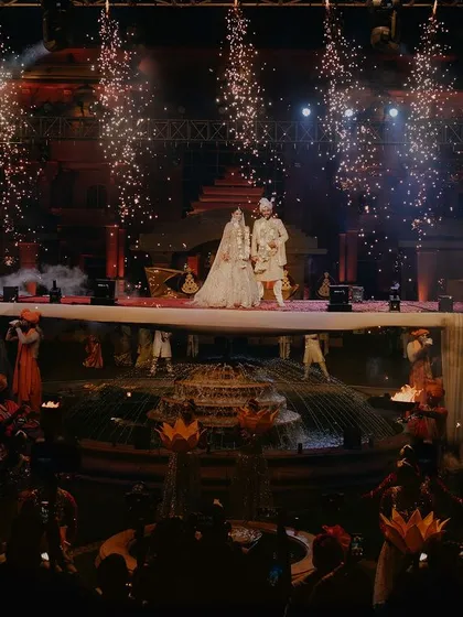 A grand stage moment for Aditya and Megha, complete with fireworks and traditional performers. This shot captures the scale and theatricality of a lavish Sangeet or reception night.
