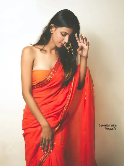 A graceful pose in a vibrant red saree, with the model's hand gently touching her traditional nose ring.