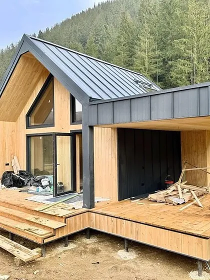 A modular A-frame house during the construction phase. The structure is nearly complete, showcasing the combination of wood and metal materials that give it a modern yet rustic look.