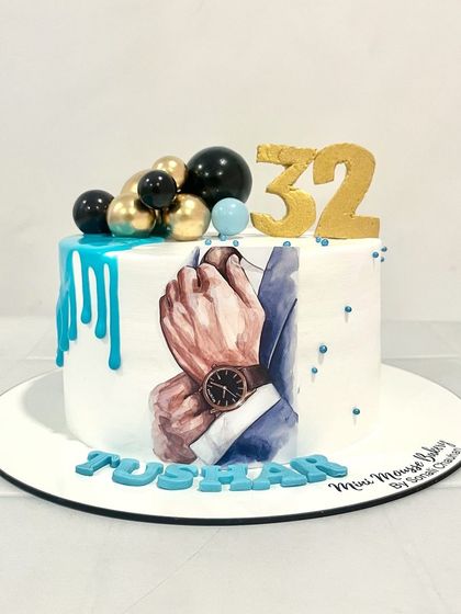 A bold and classic cake designed for him. This cake features a hand-painted image of a suit and watch, a teal drip, and a '32' topper for a stylish birthday celebration.