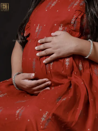 A close-up shot focusing on the hands cradling the bump, highlighting the texture of the modern red dress.