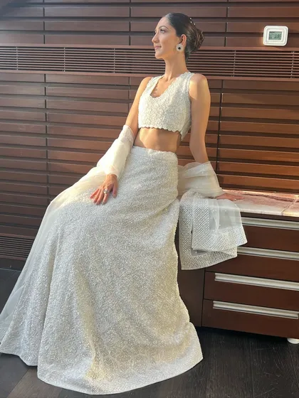 A full-length view of the client in her white lehenga, her sleek bun providing a sophisticated counterpoint to the detailed outfit.