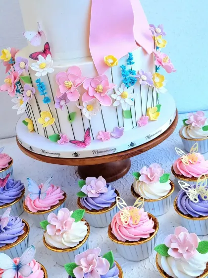 A close-up of the floral cake and matching cupcakes. The cupcakes are topped with pink, purple, and white buttercream swirls and delicate sugar flowers.