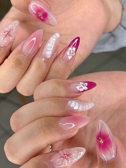 An intricate and beautiful set with pink aura nails, 3D flowers, and delicate white textured details.