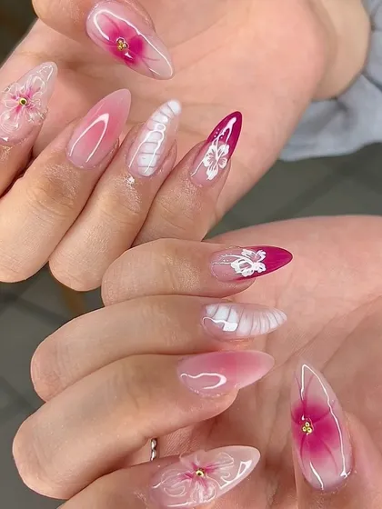 An intricate and beautiful set with pink aura nails, 3D flowers, and delicate white textured details.