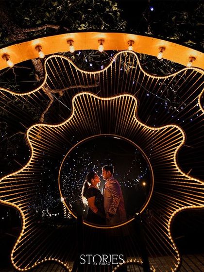 Framed within a stunning, illuminated gear-like structure at their Sangeet, the couple is lost in their own world. This creative shot captures the magic and unique decor of their celebration night.