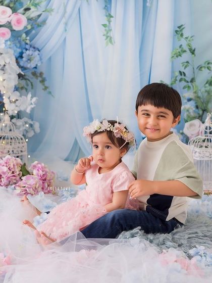 A wider shot of the sibling duo in their magical floral setting. The brother's gentle smile as he sits with his sister is heartwarming.
