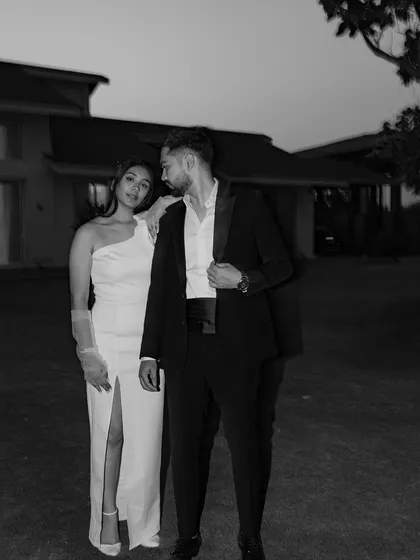 A chic and moody black and white portrait. The couple's formal attire and the subtle, knowing glance they share create a sophisticated and timeless image with a touch of old-world glamour.