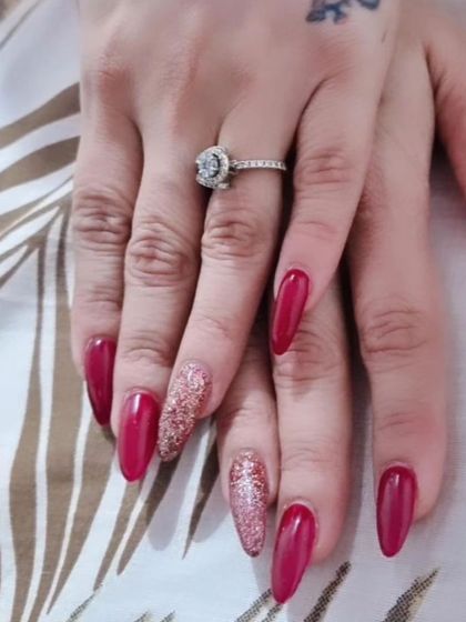 A glamorous set of long, almond-shaped nails in a deep magenta, with two accent nails fully covered in sparkling rose gold glitter.