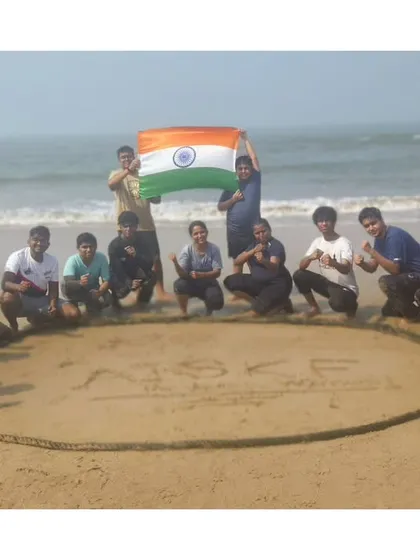 Our identity, etched in the sand. Students gather around our federation's name after a tough but rewarding beach training session, holding the Indian flag high.