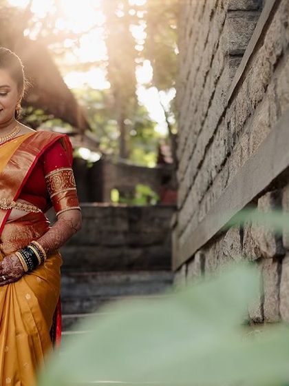 A bride in a yellow and red saree, the sunlight catching her as she walks down the stone steps.