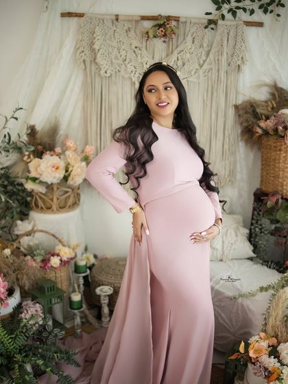 A radiant solo portrait of a mother-to-be in a lovely pink gown. The pearl headband adds a touch of elegance to the soft, romantic look.
