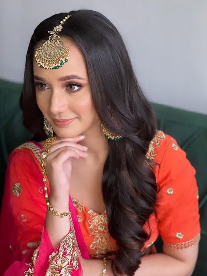 Soft, side-parted waves frame the face beautifully. This is a classic hairstyle for any wedding event, providing a touch of glamour that complements the traditional tikka and jewelry.