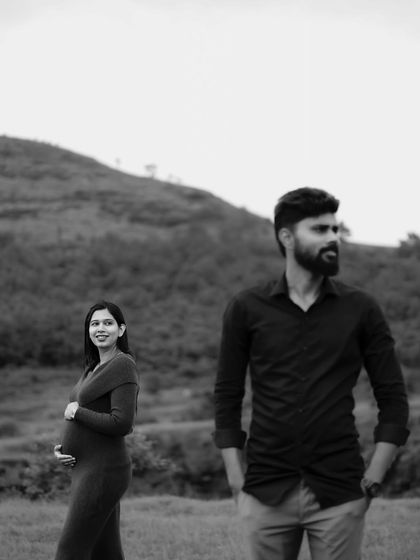 A striking black and white portrait with the dad-to-be in the foreground and the mom-to-be smiling in the background. The composition creates depth and a sense of story.