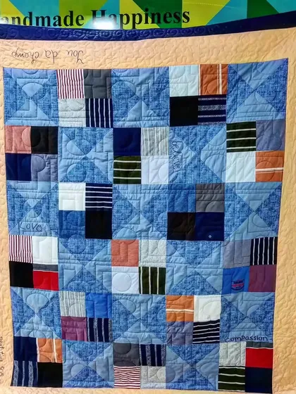 A memory quilt made from denim and t-shirt scraps, featuring hand-embroidered personal phrases that add a unique, sentimental touch.