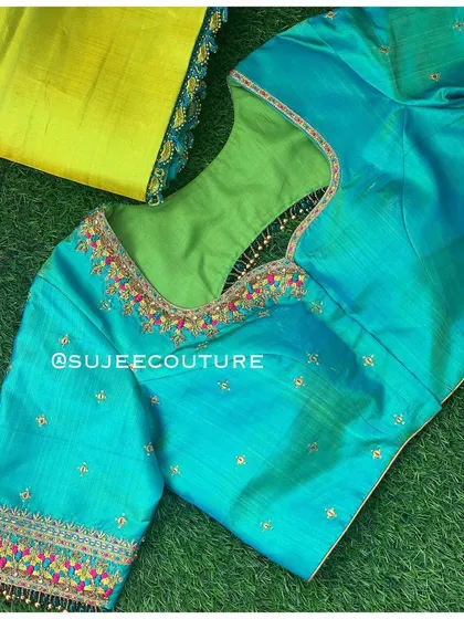 The front of the teal blouse, showing the simple neckline that allows the colorful sleeve embroidery to stand out. The blouse is paired with a contrasting lime green lining.