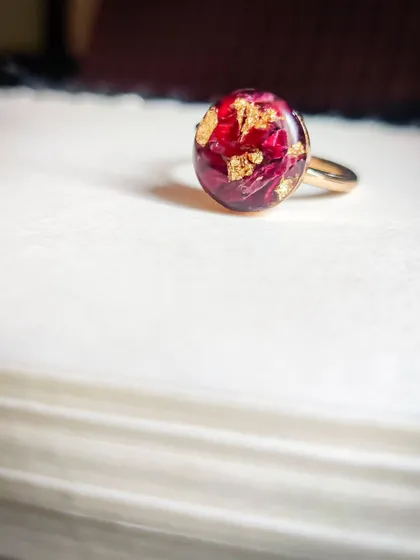 Another look at the delicate rose petal ring. The deep red of the petals contrasts beautifully with the shimmering gold flakes, all captured in a glossy resin dome.