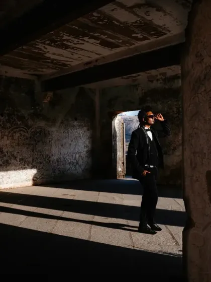 A solo portrait of the groom using strong directional light streaming into a rustic, stone room. The shadows create a moody and contemplative atmosphere, highlighting his sharp silhouette and adding a touch of cinematic drama.