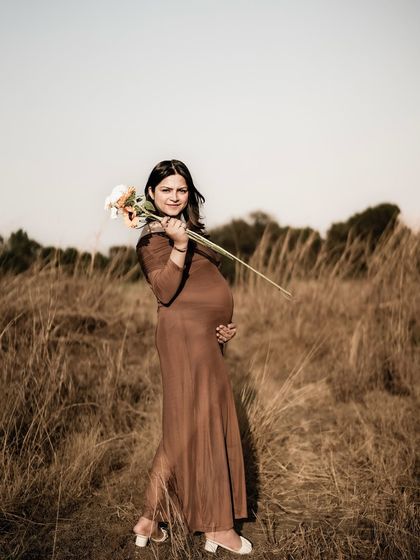 A graceful portrait of the mom-to-be in a field, holding a single flower to her shoulder. The composition is elegant and artistic.