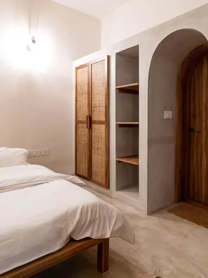 A minimalist bedroom with an arched wooden door and a rattan-fronted wardrobe. The clean lines and natural materials create a serene and uncluttered sleeping space.
