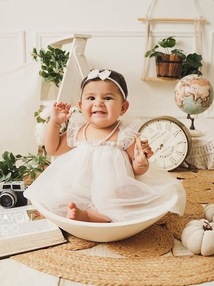 A beautiful, angelic first birthday setup in all white and natural tones. The birthday girl waves happily from her bowl.