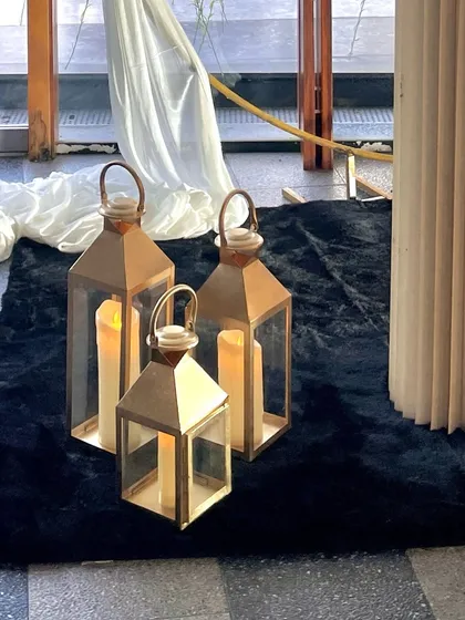 Detail shot of elegant brass lanterns with pillar candles, placed on a black rug as part of an event's decor.