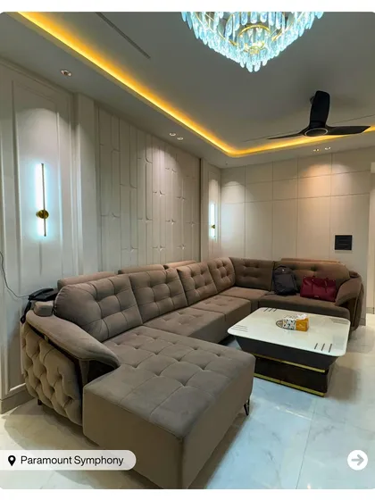 This spacious living room is designed for comfort with a large L-shaped sectional sofa. The coffered ceiling with concealed lighting and a modern chandelier adds a touch of grandeur.
