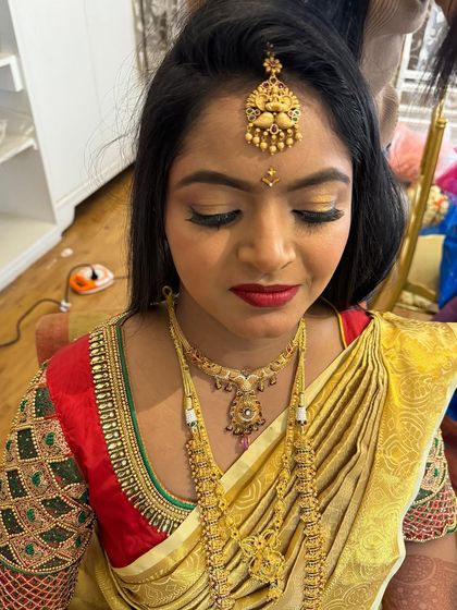 A detailed close-up of the bridal makeup. The golden eyeshadow and bold red lip are classic choices that perfectly complement the traditional gold jewellery and silk saree.