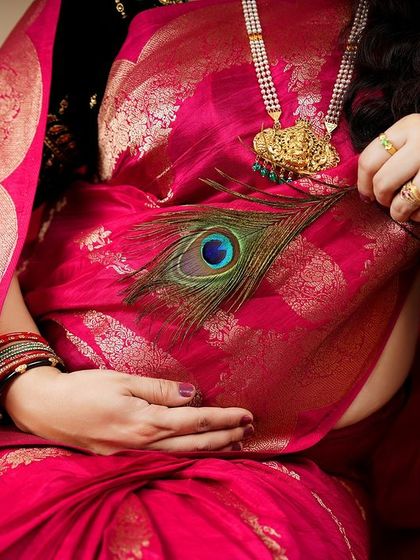 A close-up detail shot from a traditional shoot, featuring a peacock feather resting on the baby bump. This small detail adds a layer of symbolism and beauty to the portrait.