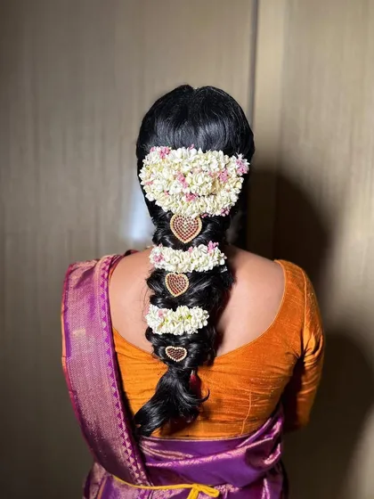 A unique take on the South Indian bridal braid, this style features sections of jasmine flowers interspersed with heart-shaped gold accessories. It's a modern and personal touch on a traditional hairstyle.
