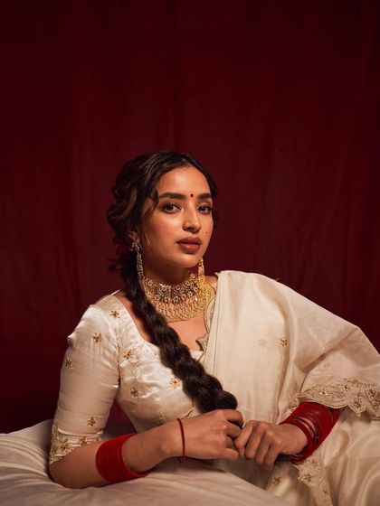 A classic portrait inspired by traditional Indian paintings. The model's pose, the rich red background, and the white and gold saree create a look of timeless beauty and cultural richness.