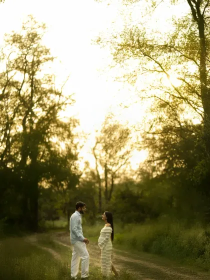Standing together under the open sky, surrounded by trees. This wide shot captures the couple in a beautiful, natural landscape, symbolizing their shared journey and the miracle of life.