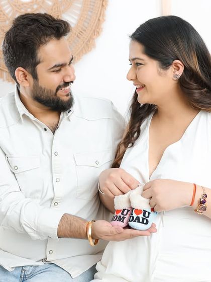 This bright and airy photo captures the couple's joy as they look at a pair of baby booties together in our boho-themed studio.