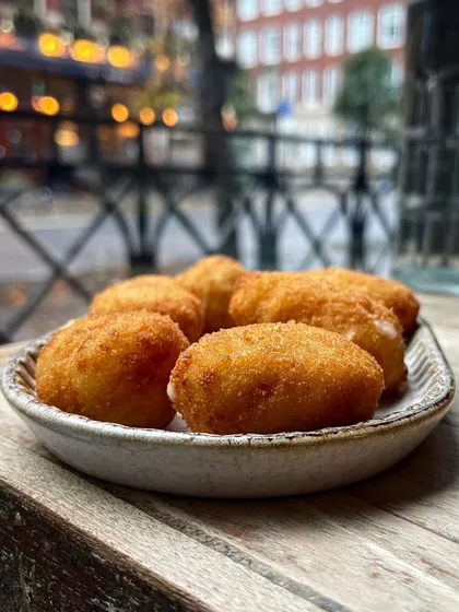 A plate of crispy fried croquetas from Iberica. The outdoor setting and natural light give the shot a relaxed, casual tapas bar feel.
