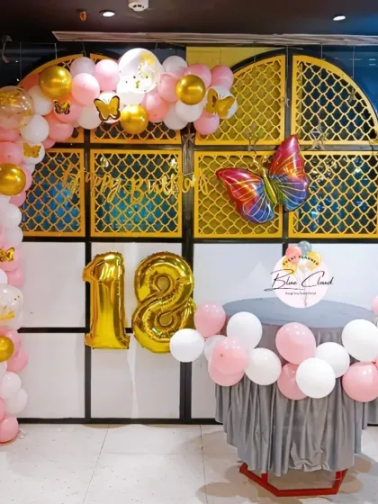 An 18th birthday celebration with a pink, white, and gold balloon arch and a large butterfly foil.