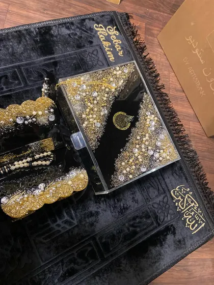 A top-down view of my trending black and gold Islamic gift set. This luxurious collection includes a personalized prayer mat, a resin Quran box, and a matching Quran holder, all heavily embellished for a grand look.
