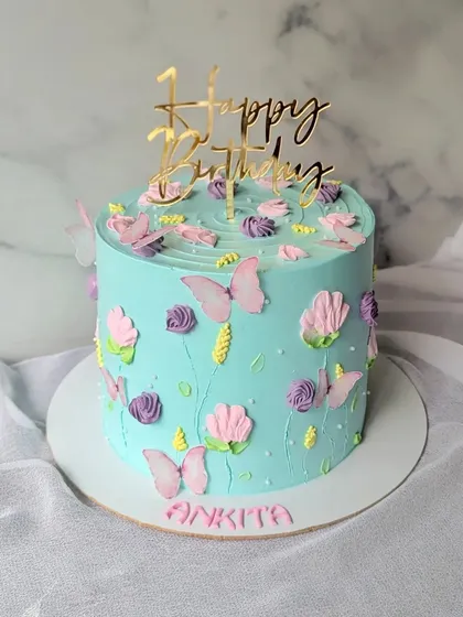 A simple floral cake in pretty pastel colors. The light blue buttercream is decorated with piped flowers and delicate butterflies.