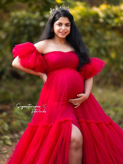 The vibrant red of the gown contrasts beautifully with the natural green background in this outdoor portrait.