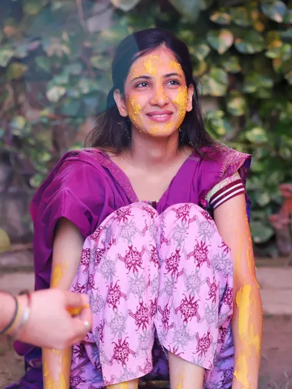 A candid shot of the bride during her Haldi ceremony, with a family member's hand just visible. It creates a sense of interaction and the communal nature of the ritual.