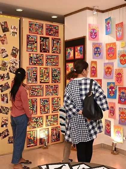 Guests at our exhibition explore the diverse collection of student work, from colorful masks to intricate collages. The entire studio is transformed into a professional gallery space for the event.