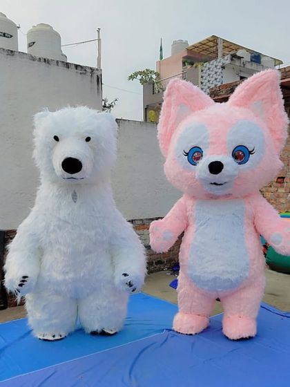 A full-length photo of the white polar bear and pink fox fur mascots standing together. These custom animal characters are made with soft, high-quality fur.