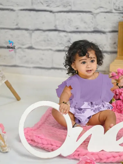 A sweet first birthday photo with a 'One' sign and a lovely pink and purple theme.