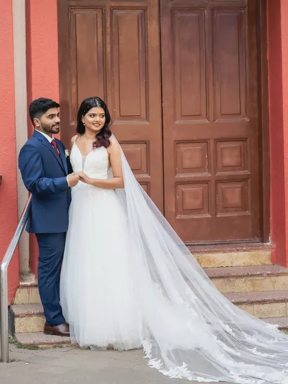 A full-length shot showcasing the bride's stunning gown and long, flowing veil. Her hair is styled in soft waves, and her makeup is classic and elegant.