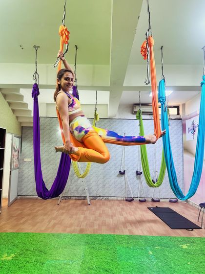 Posing with a smile because finding your balance in the air is a joyful achievement. This seated aerial pose works on core stability and leg strength, all while you feel like you're floating on a swing.