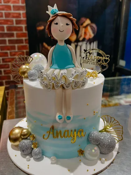 A full view of the doll cake, featuring a blue and white watercolor effect and gold and silver decorative balls.