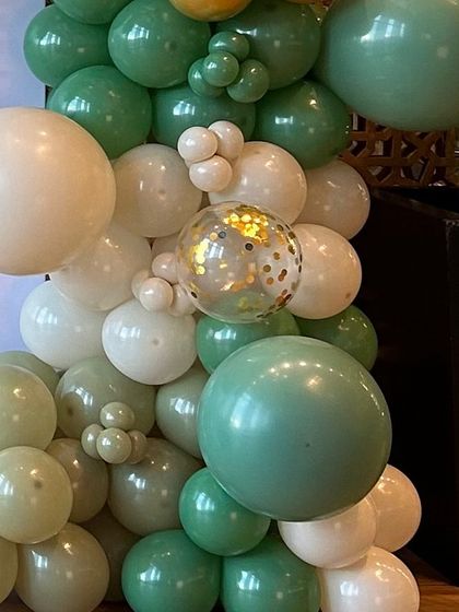 An organic balloon cluster featuring sage green, off-white, and a gold confetti balloon. This combination adds a touch of elegance to a jungle or botanical-themed event.