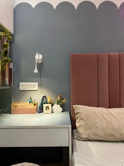 A close-up of the bedside study nook, showing the scalloped wall paint detail and the adjustable wall-mounted lamp, which provides focused light for reading without taking up desk space.