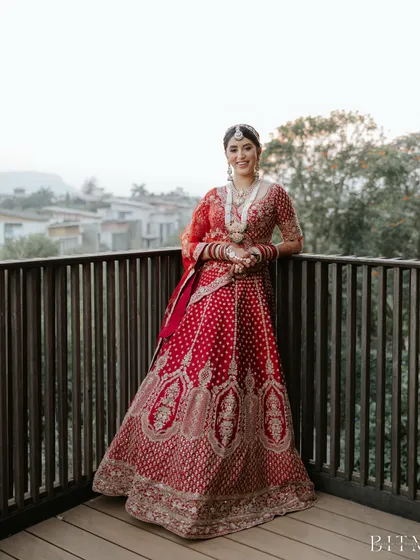 A full-length shot showcasing how a classic bridal bun completes the traditional red lehenga look, creating a silhouette of timeless elegance for the wedding day.