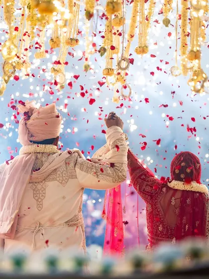 A beautiful, emotional shot from behind the couple during their varmala, with a shower of petals and a backdrop of fireworks. This captures the grandeur and intimacy of the moment.